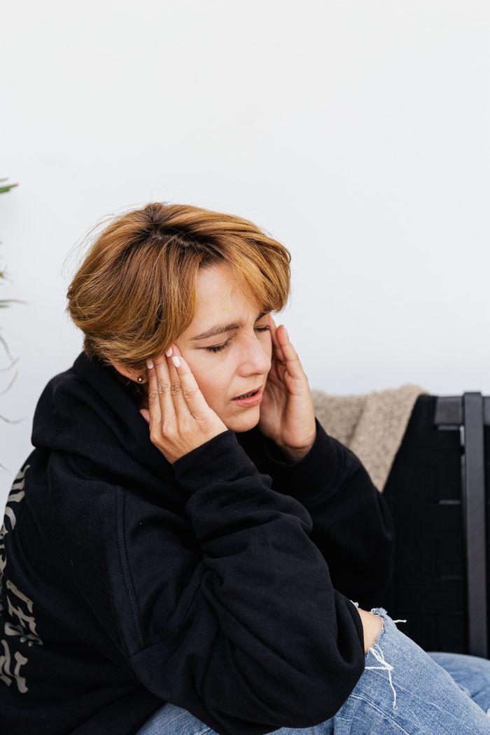Services Young woman holding head in discomfort, symbolizing stress or headache.