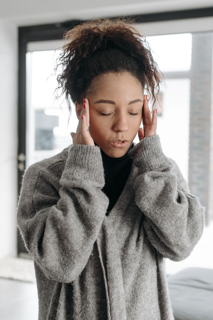 Young woman indoors showing signs of illness, touching her temples in discomfort.