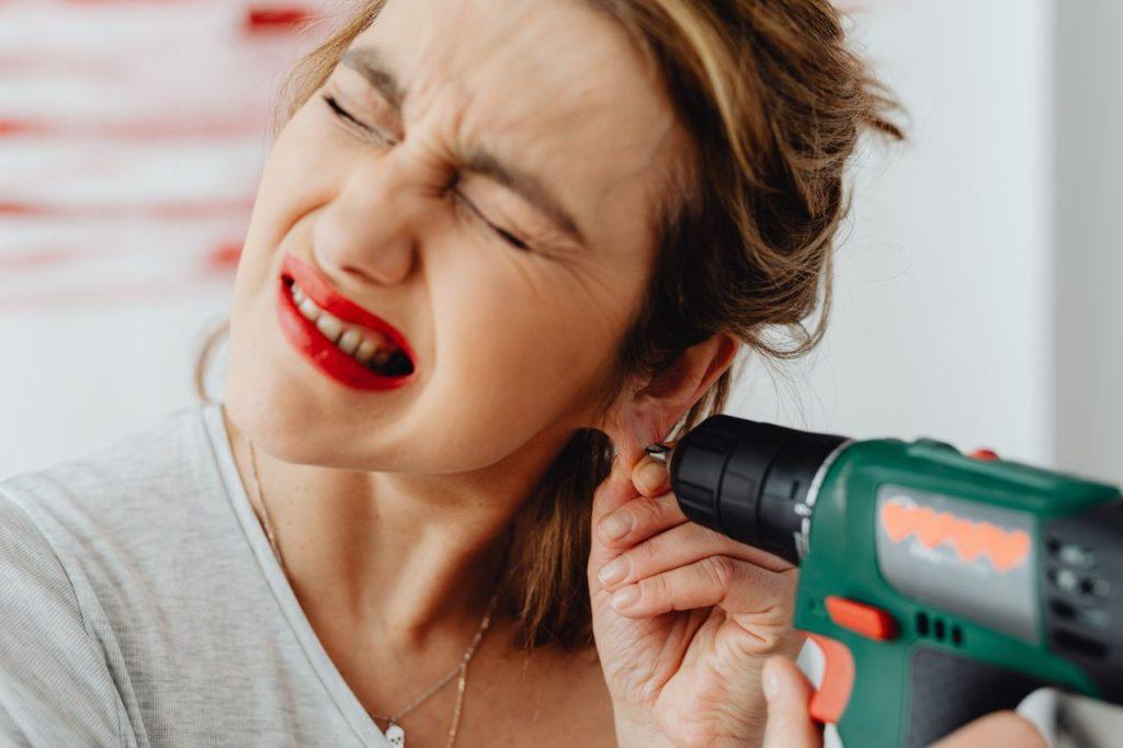 Woman's humorous expression as she uses a drill near her earring.