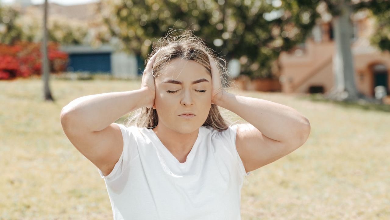 Services Caucasian woman in a park, eyes closed, holding head in pain hinting at a headache or migraine.