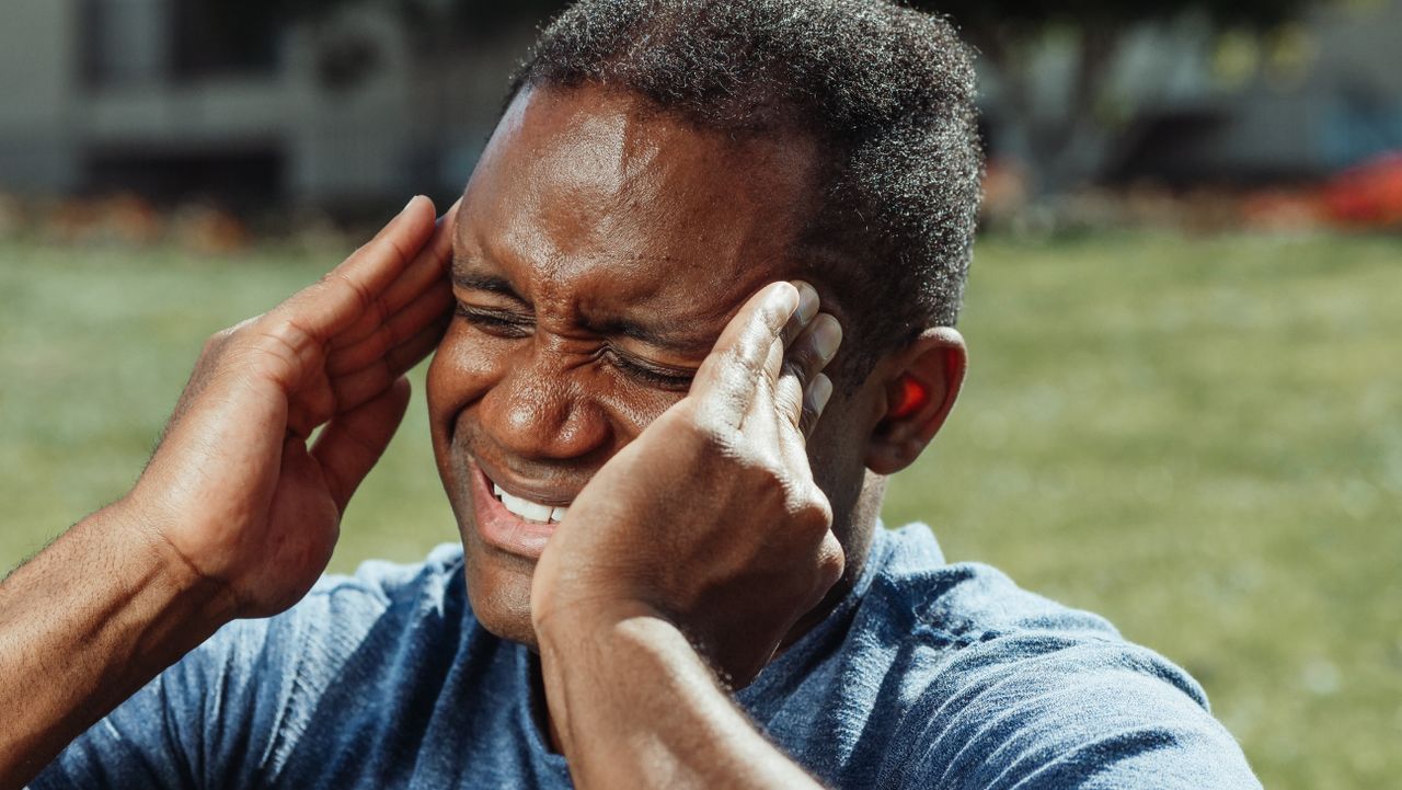 Close-up of a man with a headache holding his head in pain outdoors.