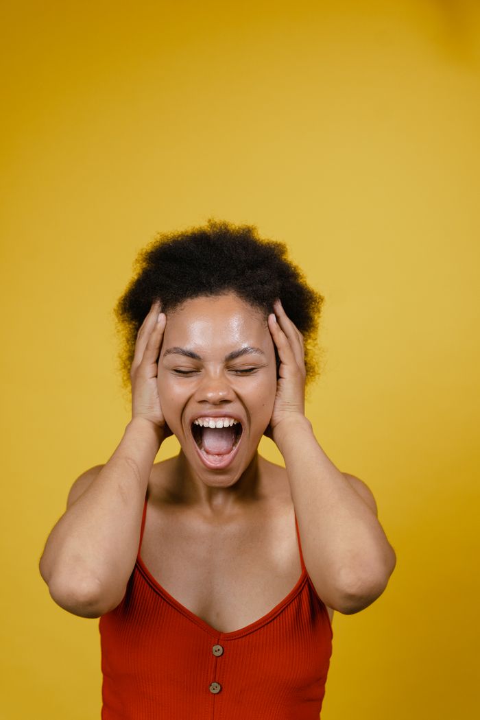 Services Young African American woman in red top expressing strong emotions in a studio setting with a vibrant yellow backdrop.